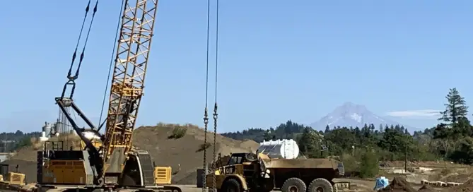Tracked crane lifting a compaction tamper over rolling grassland during a dynamic compaction project